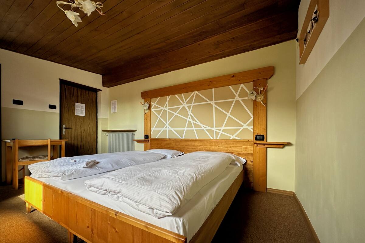 A room with two wooden beds, a wooden desk, a radiator, and a wooden ceiling.