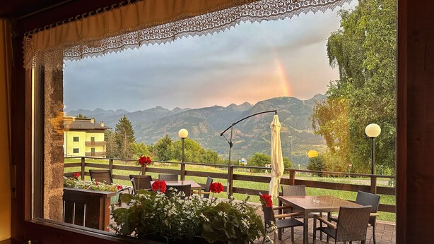 Een restaurant met terras, met uitzicht op een bergachtig landschap, inclusief een regenboog en een geel gebouw in de verte.