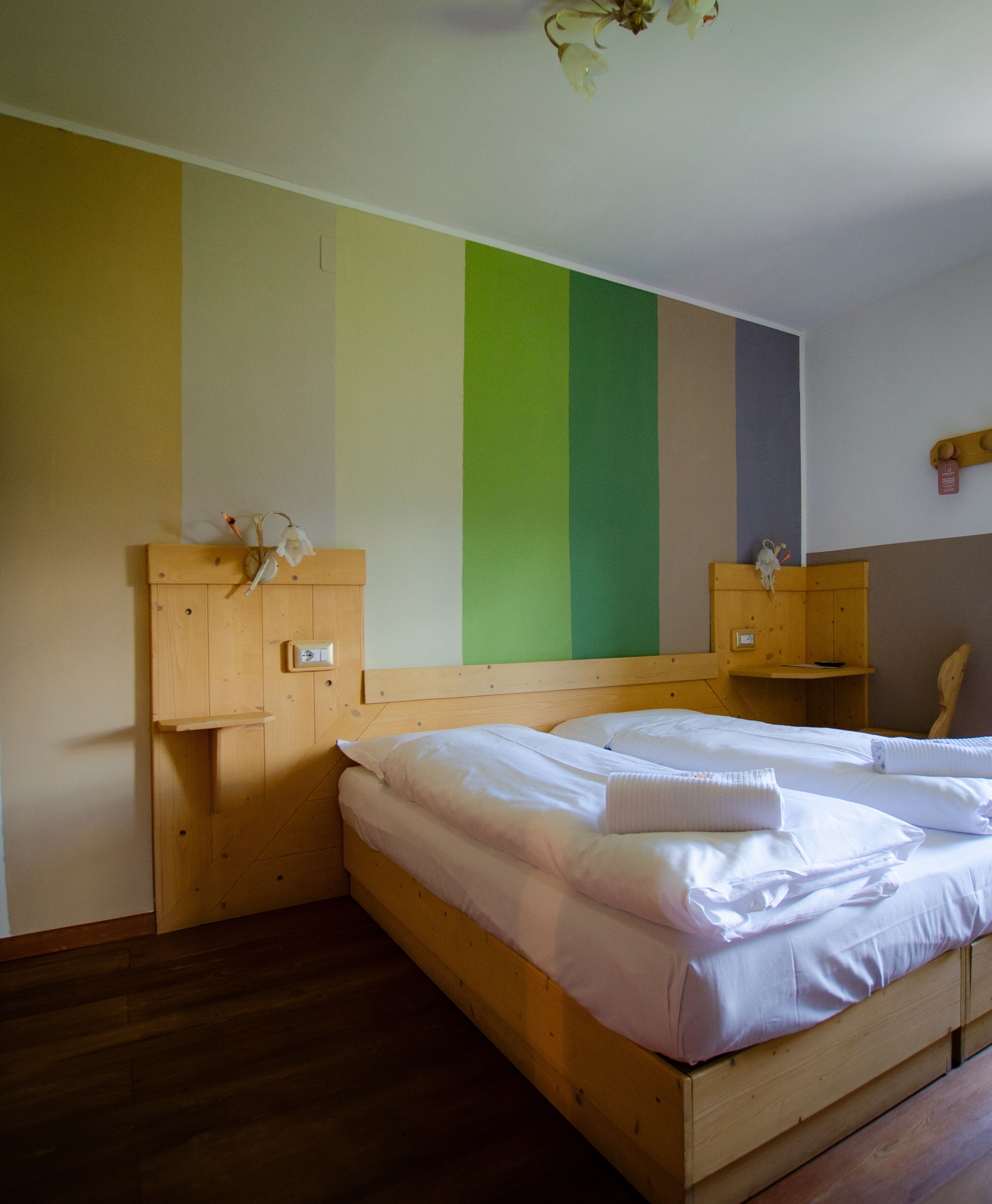 Una habitación con una cama de madera, una mesita de noche de madera, un pequeño armario de madera y una pared a rayas verticales.