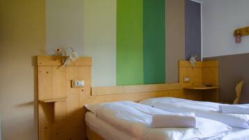 Una habitación con una cama de madera, una mesita de noche de madera, un pequeño armario de madera y una pared a rayas verticales.