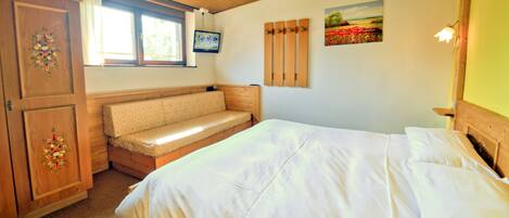A bedroom with a bed, a bench, a wardrobe, a window, and a painting.