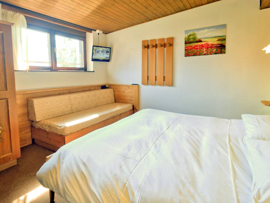 Une chambre à coucher comprenant un lit, un banc, une armoire, une fenêtre et un tableau.