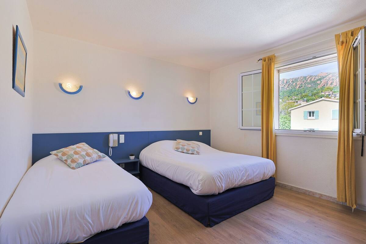 A hotel room with two beds, a bedside table with a phone, and a window with curtains.