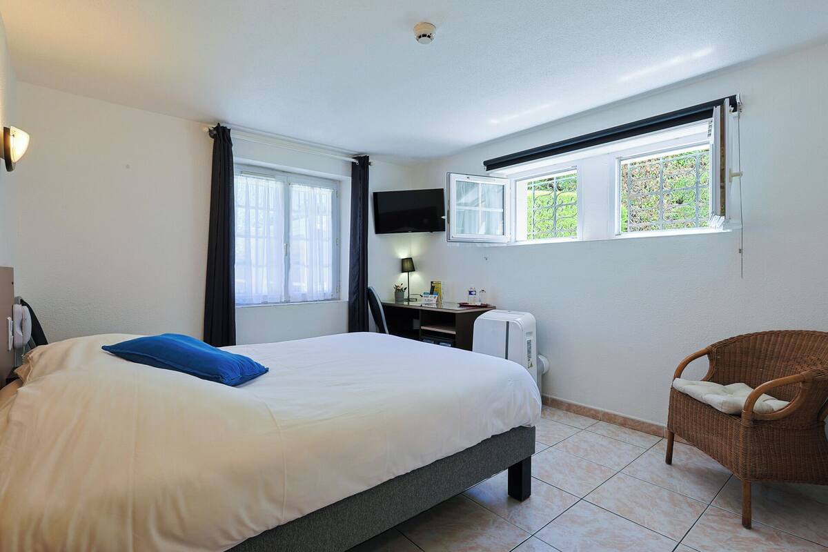 A bedroom with a bed, a desk, a chair, a TV, and windows.