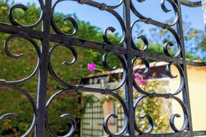 A wrought iron gate with intricate scrollwork, set against a backdrop of greenery and a building with a yellow facade. - Logis Hotel l'Esterella (Saint-Raphael)