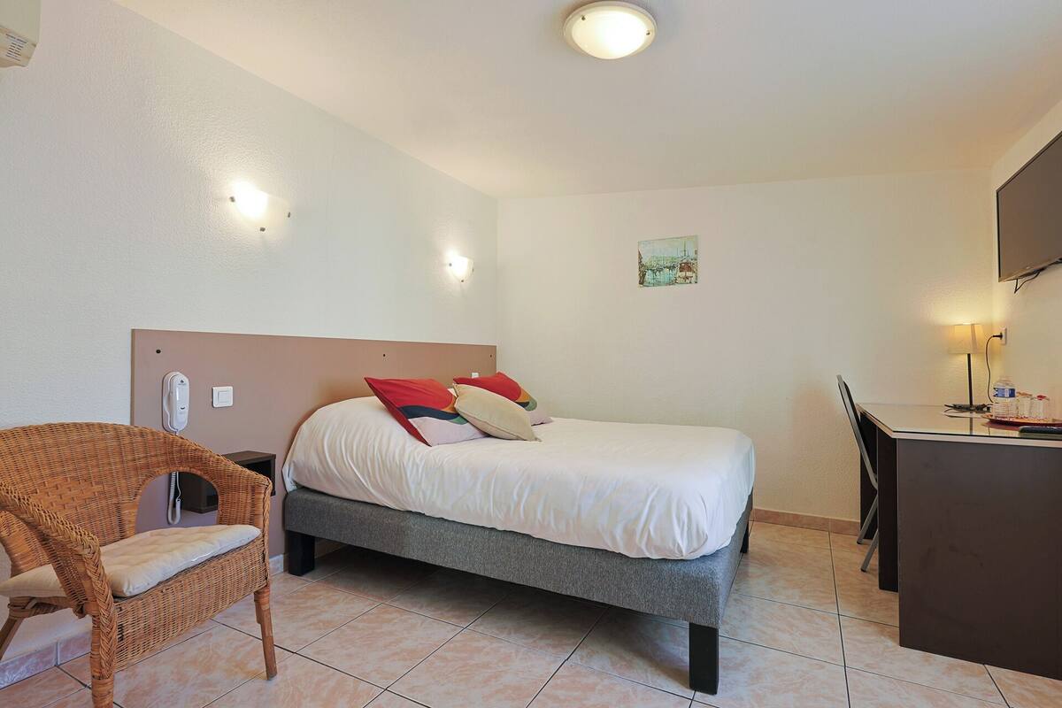 A hotel room with a bed, a chair, a desk, and a wall-mounted phone.