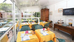 Un coin repas lumineux, avec des tables préparées pour le petit-déjeuner, un buffet en bois et un téléviseur fixé au mur.