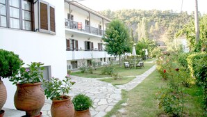 A courtyard with a stone pathway, potted plants, and a building with balconies. - Afroditi (Skopelos)