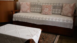 A cozy room with a wooden sofa adorned with patterned cushions, a matching white crocheted throw, and a small wooden table with a white tablecloth. - Afroditi (Skopelos)