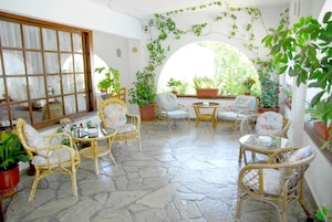 Un patio soleado con mobiliario de mimbre, plantas en macetas y suelo de piedra.