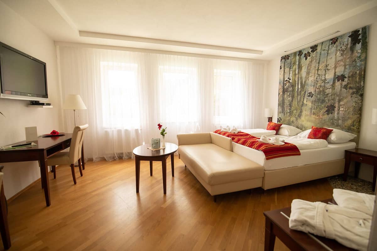 Quarto de hotel moderno com sofá-cama, escrivaninha, televisão e um quadro na parede.