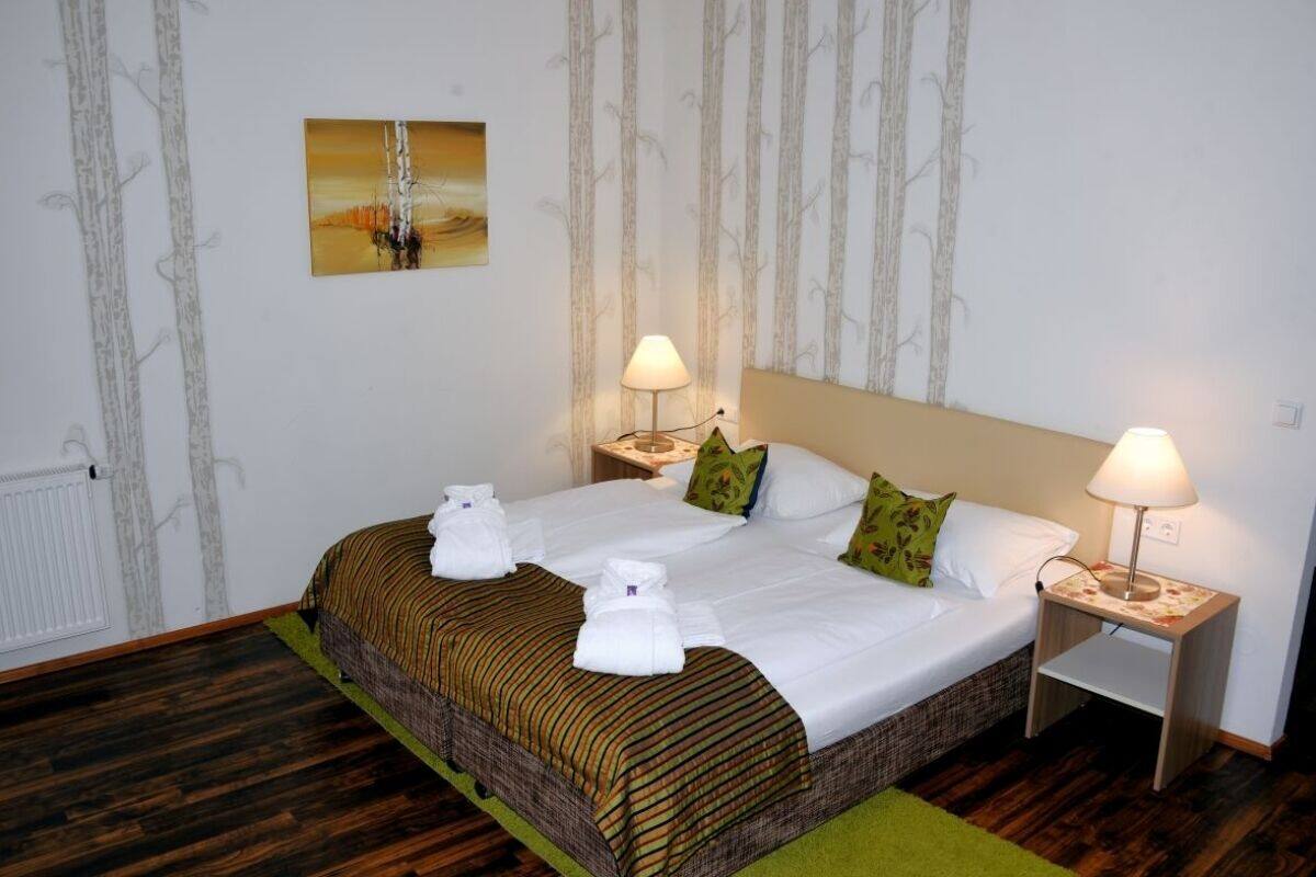 Quarto de hotel com uma cama grande, duas mesas de cabeceira com luminárias, um quadro na parede e um radiador.