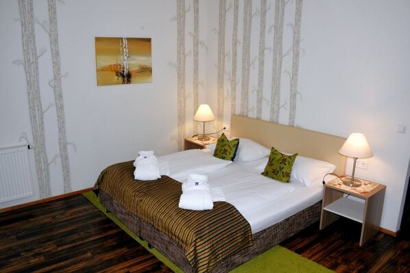 A hotel room with a large bed, two bedside tables with lamps, a painting on the wall, and a radiator.