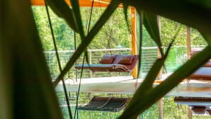 Un área de descanso con un banco acolchado y una mesita baja, con vistas a un paisaje verde exuberante a través de amplias ventanas.