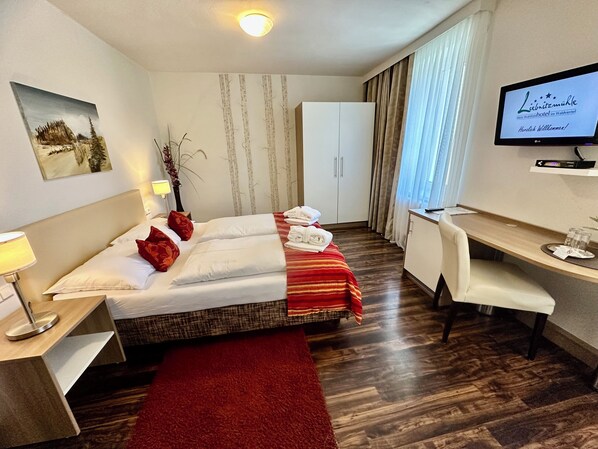 A hotel room with a bed, a desk, a TV, and a wardrobe.