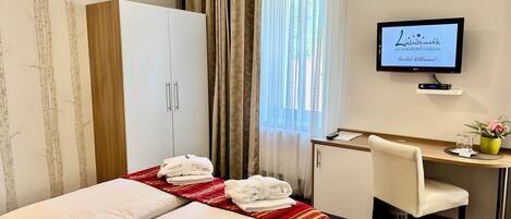 Habitación de hotel con cama, escritorio, silla y televisor mostrando un mensaje de bienvenida.