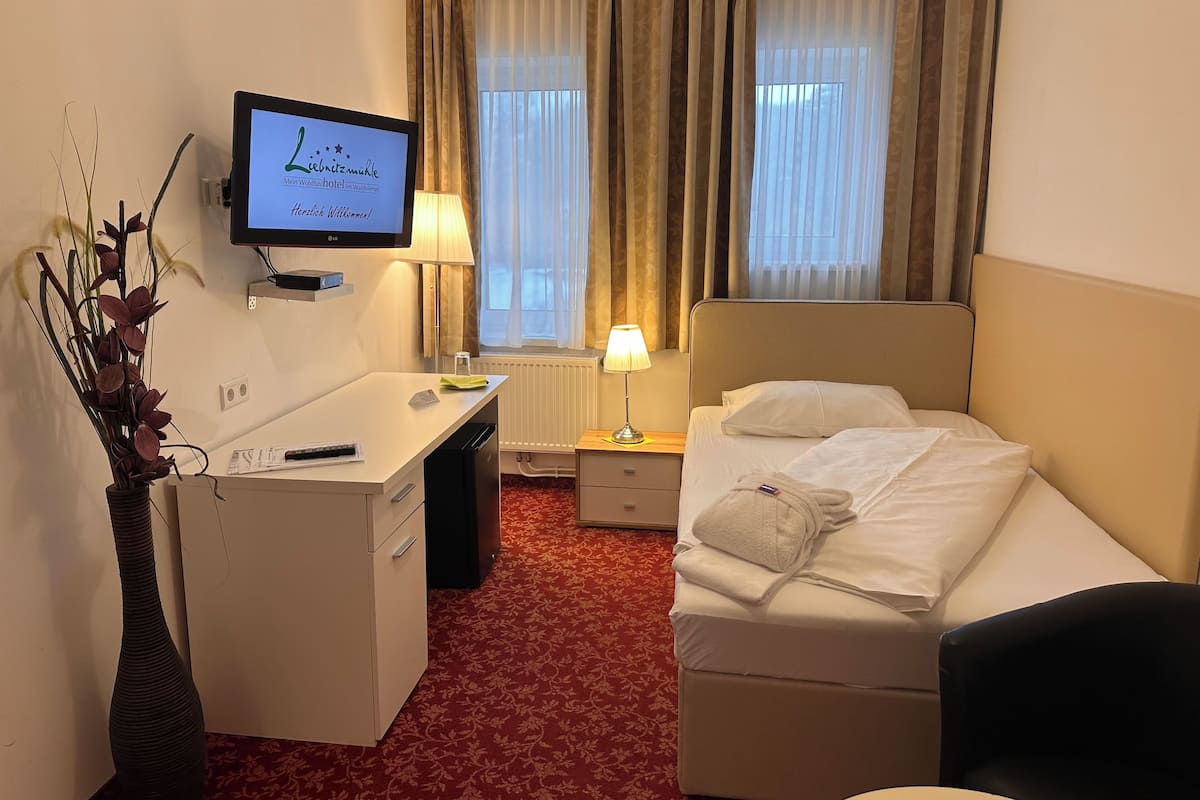 Quarto de hotel com cama, escrivaninha, televisão, luminária e um vaso com plantas.