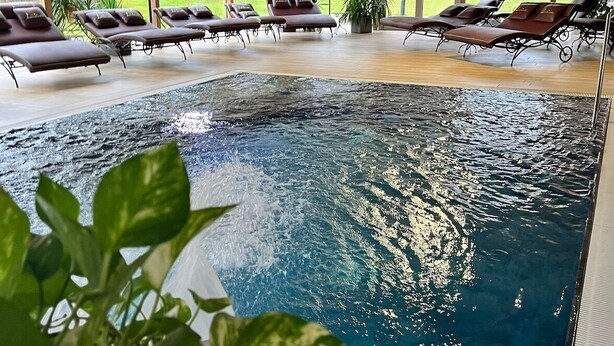 Piscina interior con sillones de descanso y vistas al exterior.