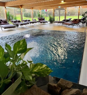 An indoor swimming pool with lounge chairs and a view of the outdoors.