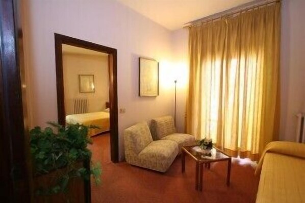 A hotel room with a sofa, a small table, a potted plant, a bed, and a large window with curtains. - Hotel Mercurio (Mercogliano)