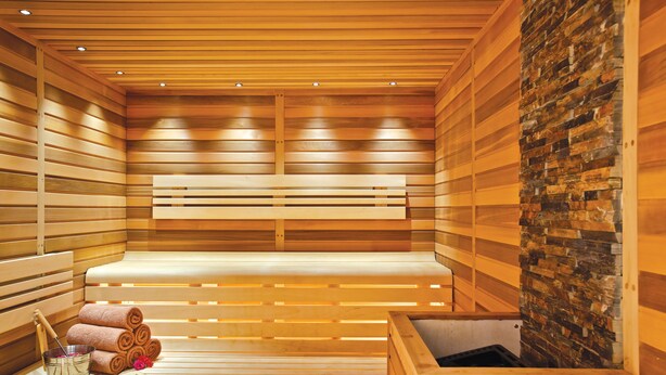A sauna with wooden benches, a stone wall, and a bench with towels and a bucket. - Karaca Otel (Izmir)
