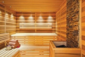 A sauna with wooden benches, a stone wall, and a bench with towels and a bucket. - Karaca Otel (Izmir)