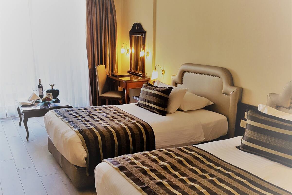 Habitación de hotel con dos camas, un escritorio con lámpara y un espejo grande.