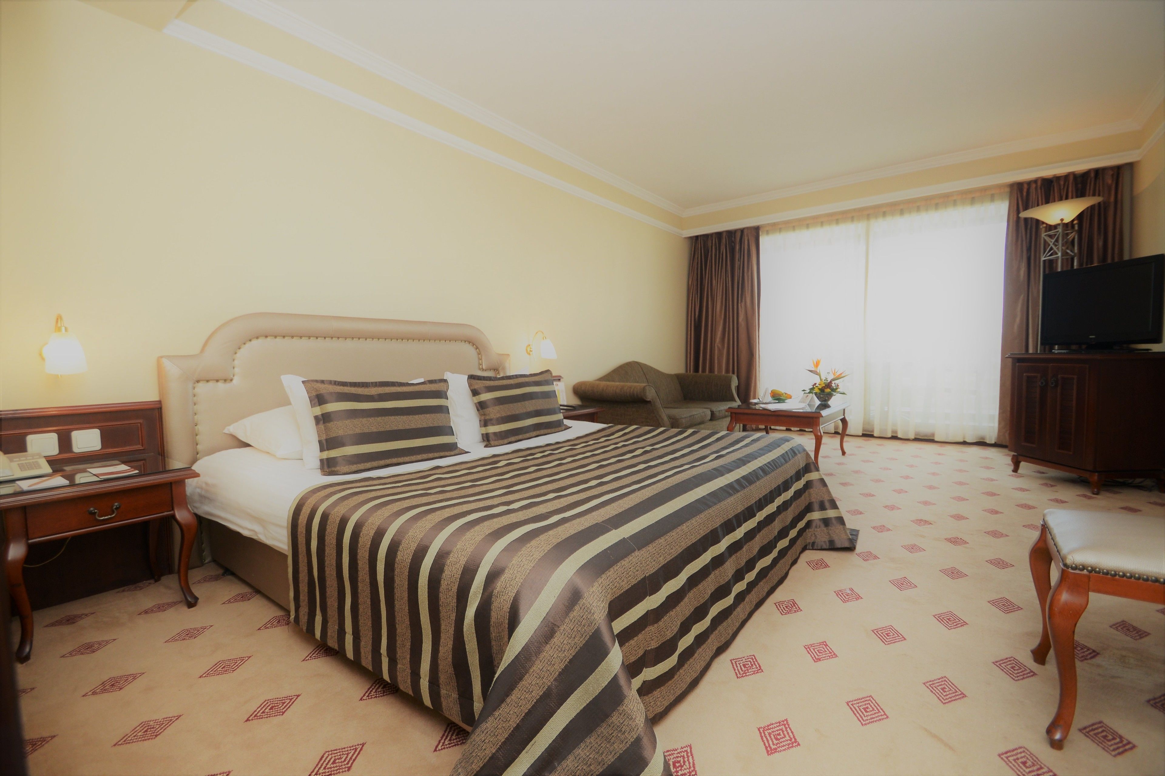 A hotel room with a large bed, a television, a desk with a lamp, and a chair.