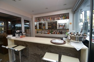 Una zona de bar con mostrador, taburetes y una variedad de botellas y vasos.