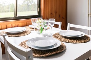 Uma mesa de jantar posta com pratos brancos, copos transparentes e um arranjo floral branco.