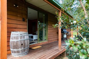 A wooden cabin with a sliding glass door leading to an interior space. A wooden barrel is placed on the porch, and a grill is visible in the background.