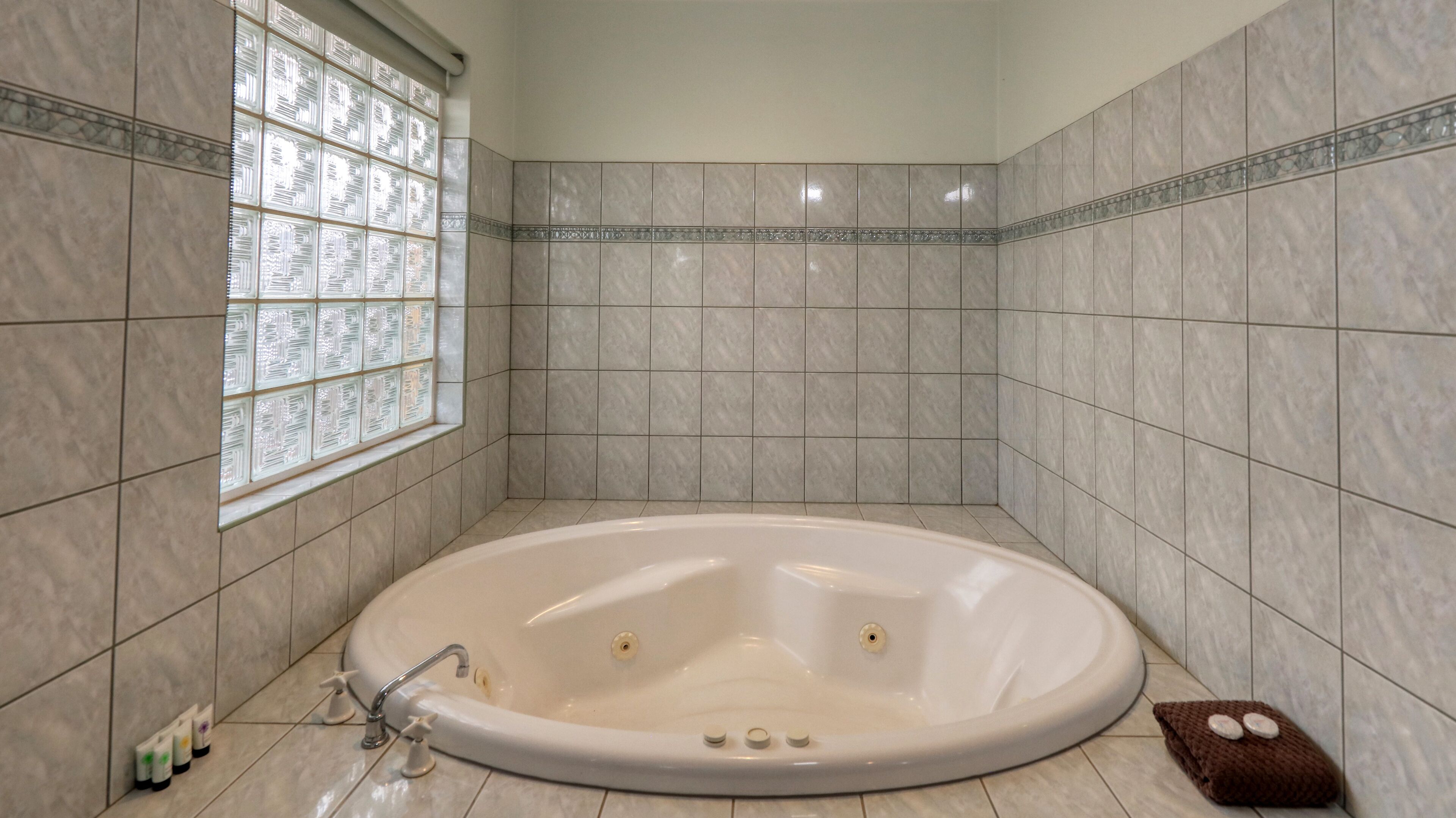 Un baño con una bañera independiente, paredes con azulejos, un ventanal con vidrio decorativo y una alfombra de baño marrón.