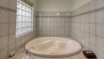 Un baño con una bañera independiente, paredes con azulejos, un ventanal con vidrio decorativo y una alfombra de baño marrón.