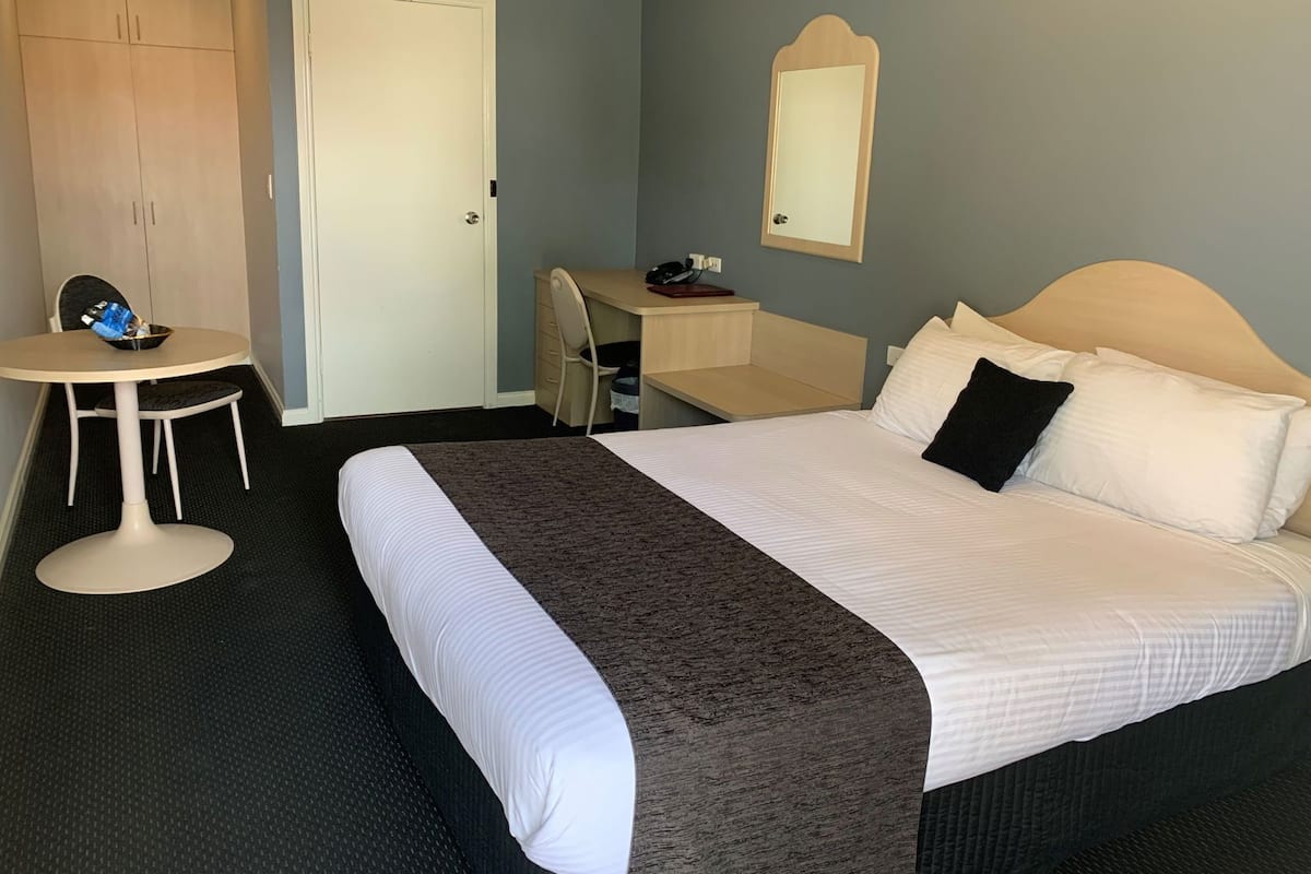 Quarto de hotel com cama, escrivaninha, cadeira, mesa pequena e guarda-roupa.