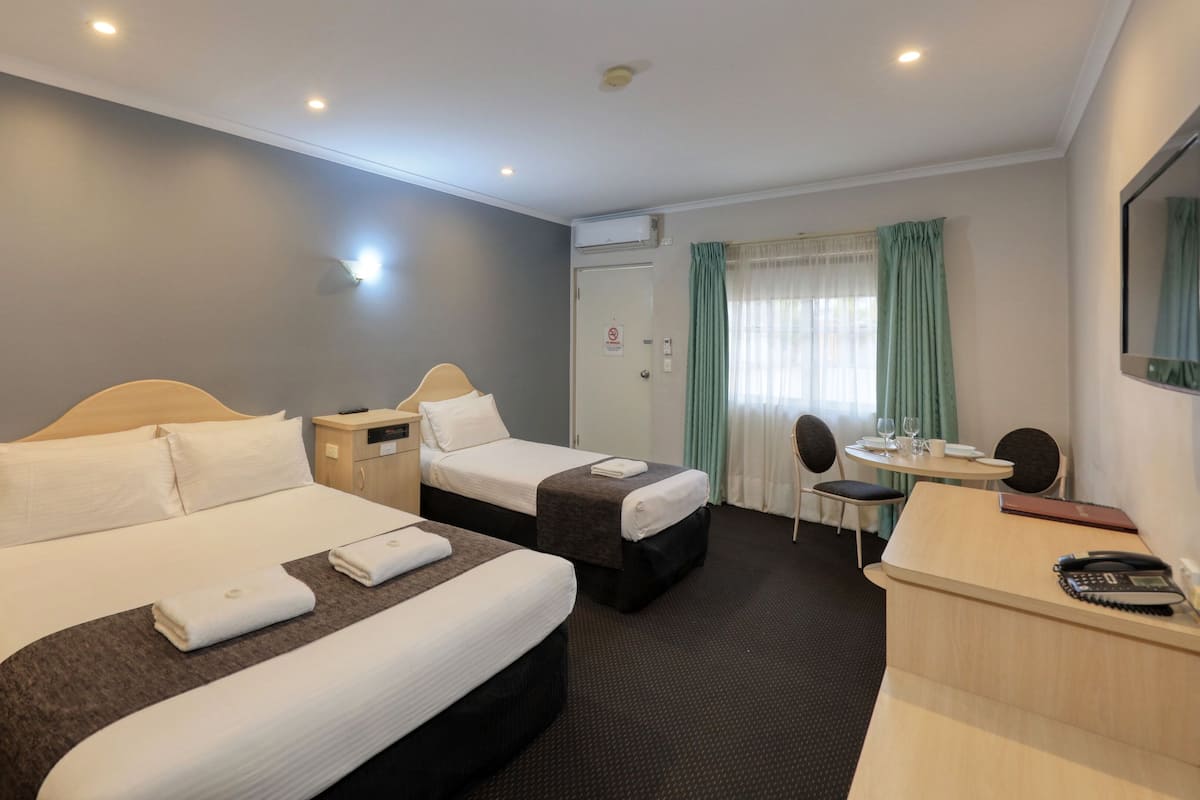 Quarto de hotel com duas camas, uma escrivaninha, uma cadeira e uma mesinha.