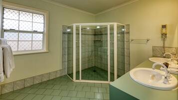 Een badkamer met een glazen douchecabine, een wastafel met spiegel en een raam met metalen hor.