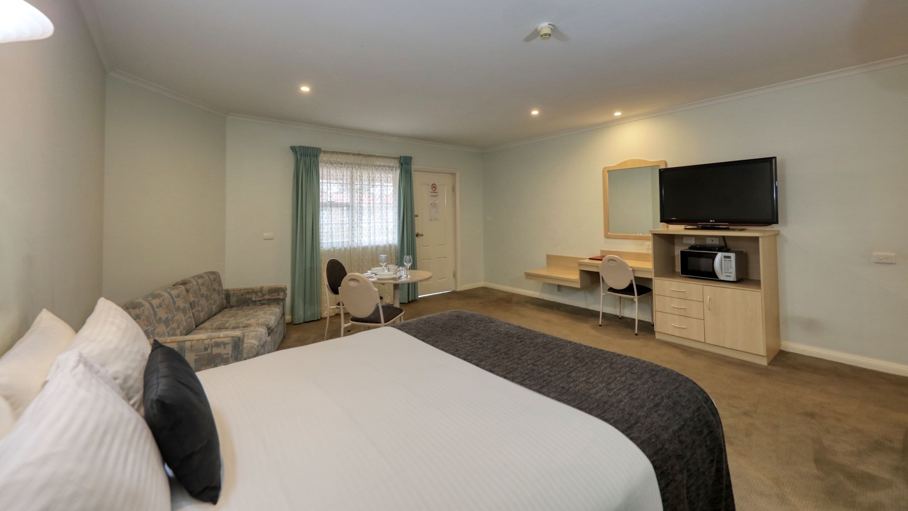 A hotel room with a large bed, a desk, a television, and a microwave.