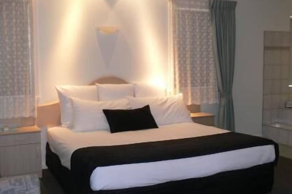 Quarto de hotel com cama, mesas de cabeceira e janela com cortinas.