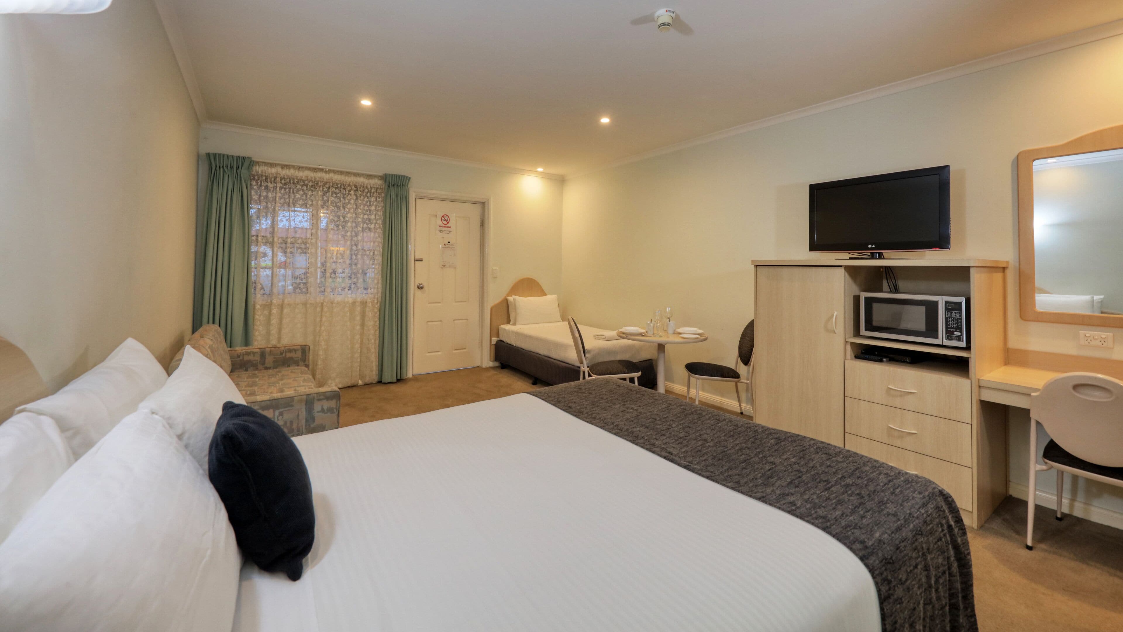 Una habitación de hotel con cama, escritorio, silla, televisor y microondas.