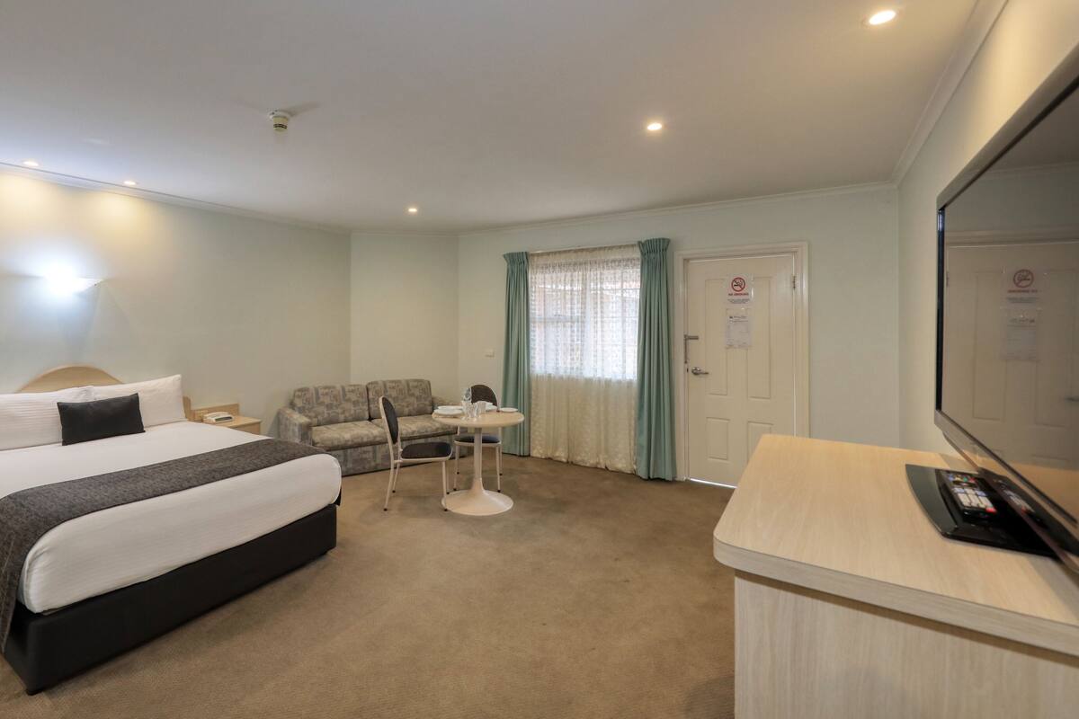 Quarto de hotel com uma cama, um sofá, uma mesinha e uma televisão.
