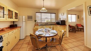 Une cuisine compacte avec un coin repas, comprenant une table ronde pour quatre personnes, un réfrigérateur, un four à micro-ondes et un évier.