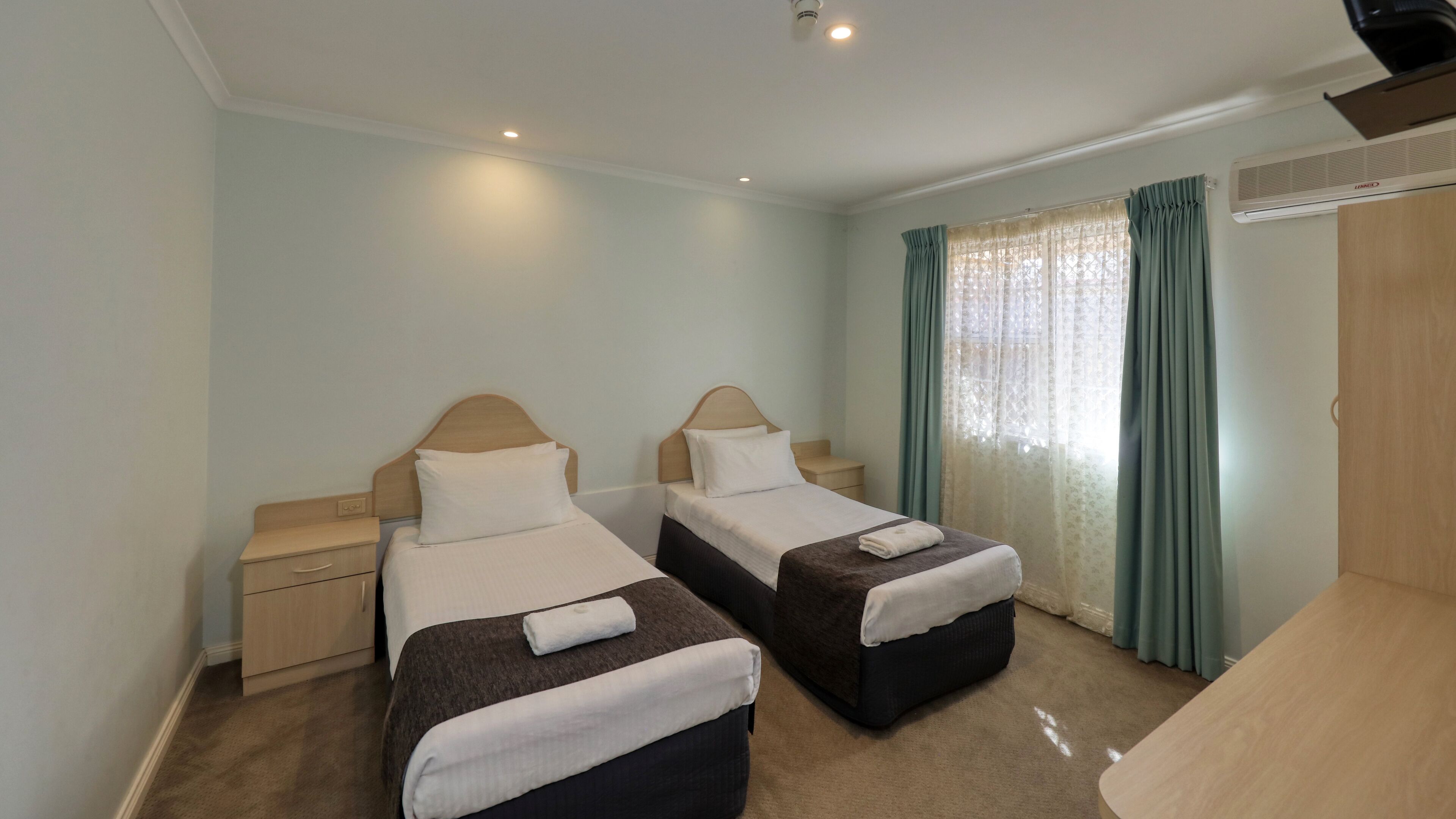 Una habitación de hotel con dos camas individuales, un armario de madera, un escritorio y una ventana con cortinas.