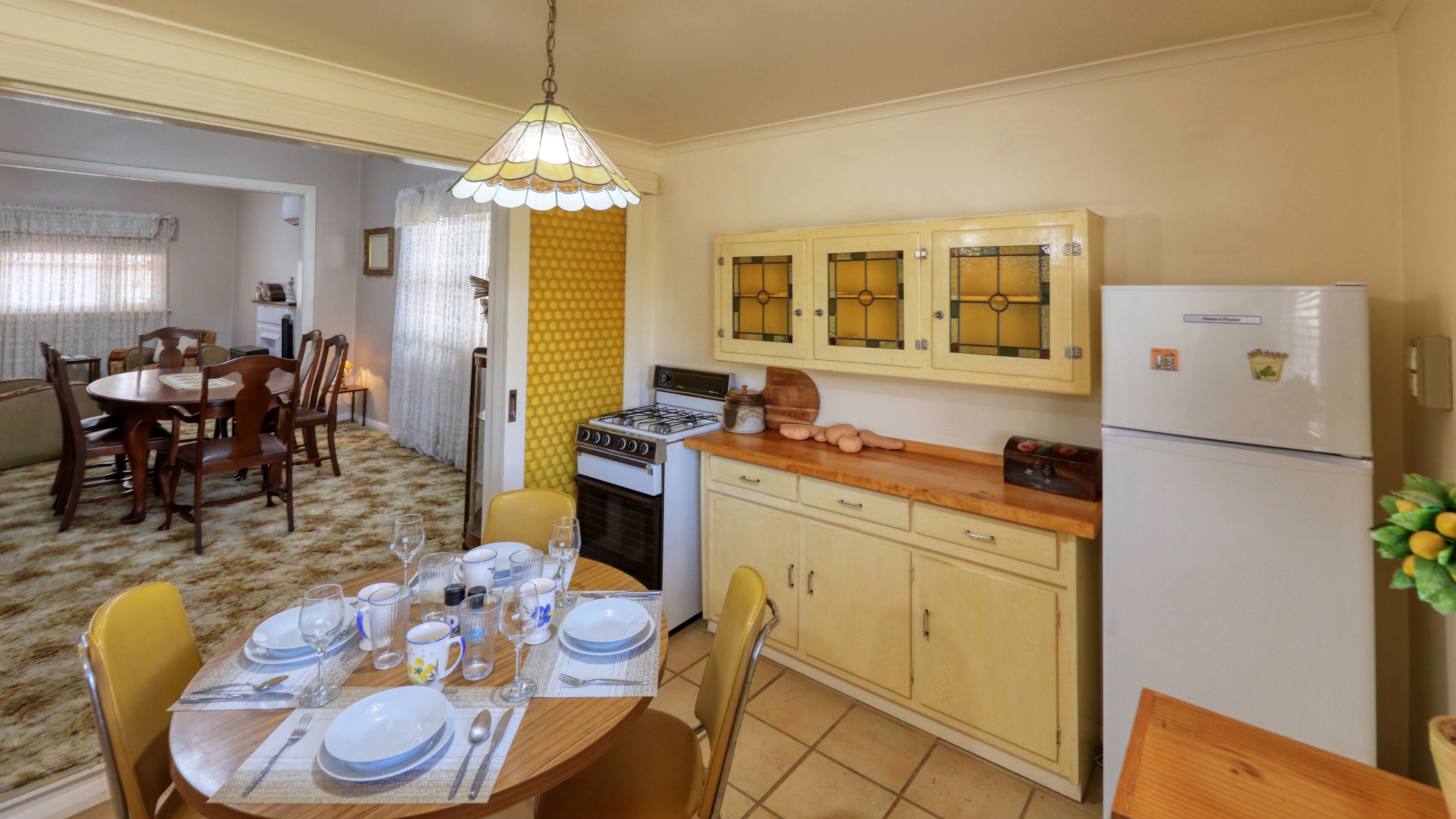 Un comedor con una mesa redonda preparada para cuatro personas, estufa y refrigerador.