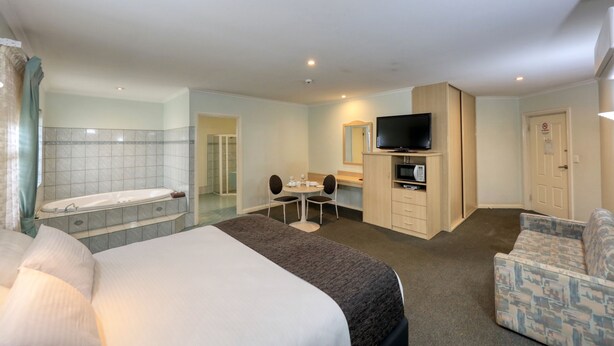 Une chambre d’hôtel comprenant un lit, un coin salon avec une table et des chaises, une télévision, un four à micro-ondes et un espace douche.