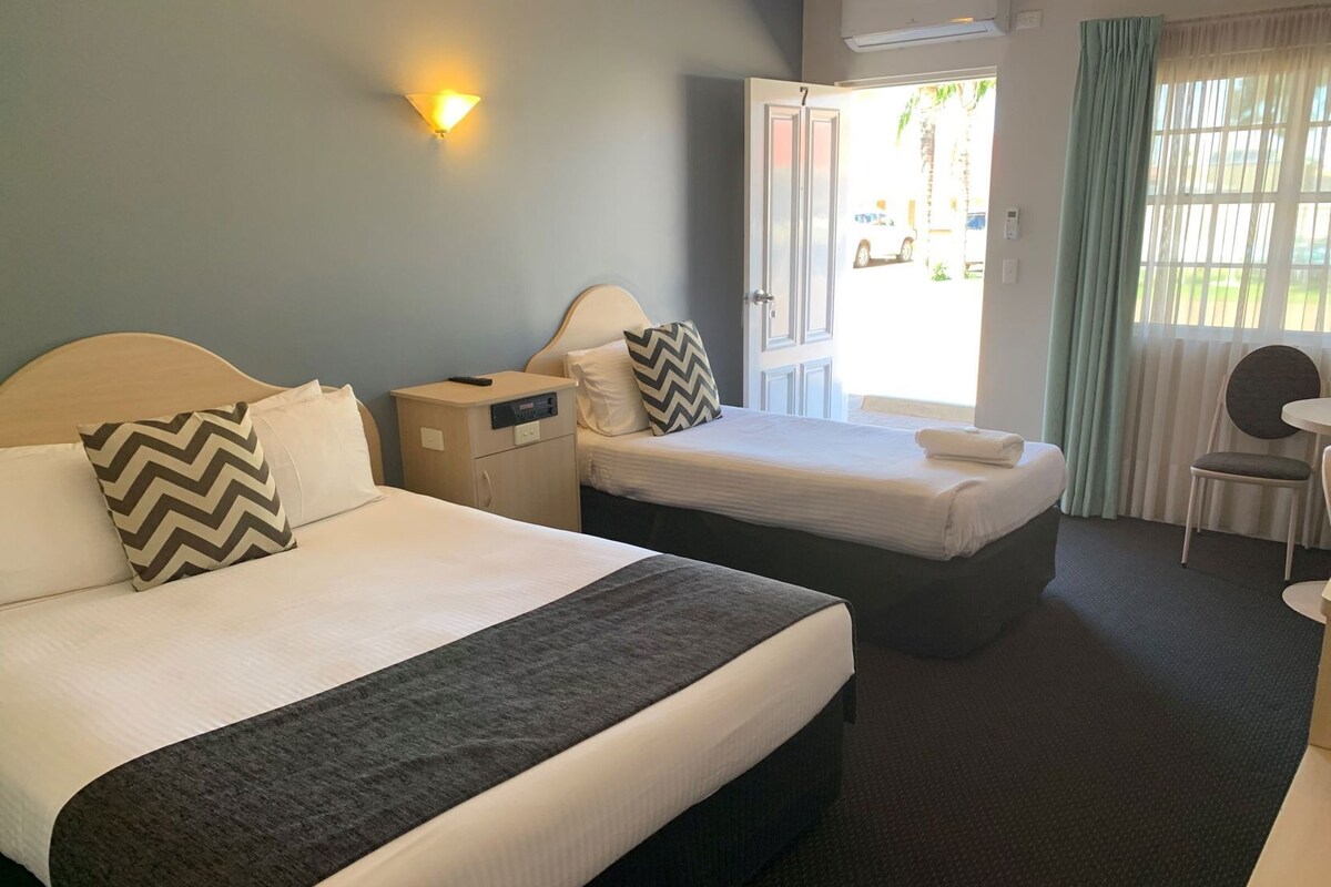 Habitación de hotel con dos camas, un escritorio, una silla, una lámpara y una ventana con cortinas.