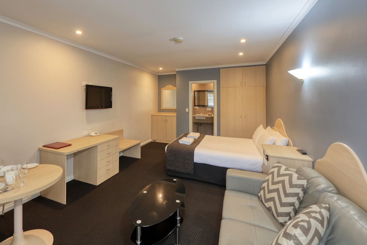 Quarto de hotel com cama, sofá, escrivaninha, cadeira, mesinha e televisão.