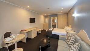 A hotel room with a bed, a sofa, a desk, a chair, a small table, and a TV.