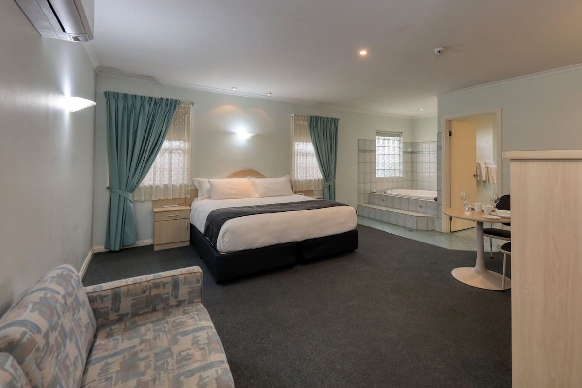 Quarto de hotel com cama, pequena escrivaninha, banheiro com banheira e área de estar.