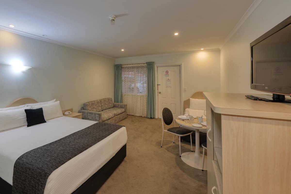 Quarto de hotel com cama, sofá, escrivaninha com cadeira, televisão e porta com placa.