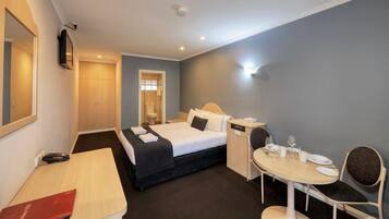 A hotel room with a bed, bedside table, chair, and a small dining table with plates and glasses.